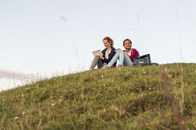 Low angle view of mother and daughter siting on hill at park against sky