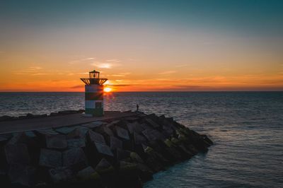 Lighthouse at sea against sky during sunset