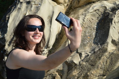 Happy woman taking selfie from camera against rock formation