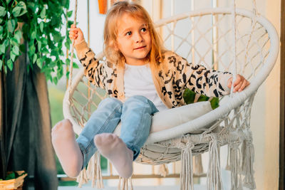 Portrait of little girl sitting in a hammock chair at home on the balcony in spring, summer sunset.