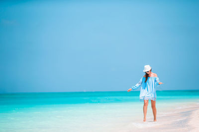 Full length of woman standing on beach against blue sky