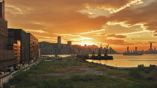 Factory by buildings against sky during sunset