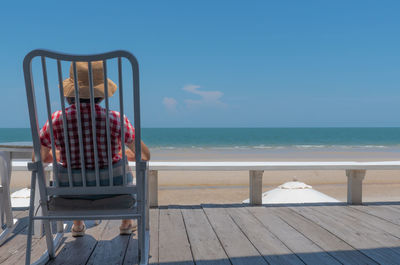 Senior woman sitting on balcony of hotel looking at blue sea and white beach in sunny day