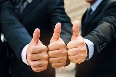 Midsection of colleagues gesturing thumbs up sign outdoors