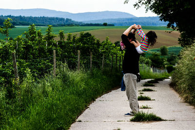 Side view of father carrying daughter on shoulder amidst plants