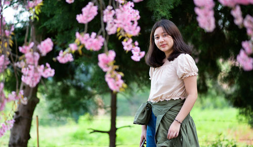 Young asian girl looks at the camera and takes pictures under a cherry blossom tree.