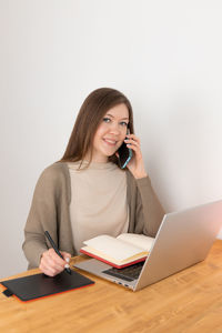 Smiling woman calling on mobile phone and looking into camera. girl makes handwritten notes