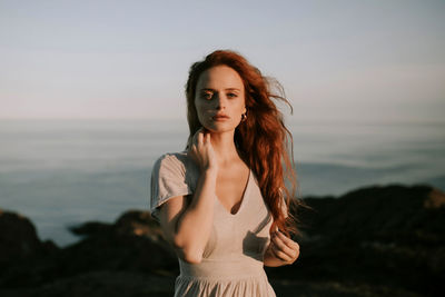 Portrait of beautiful young woman standing against sea during sunset