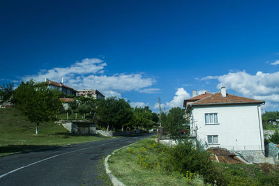 Houses by road amidst buildings against blue sky