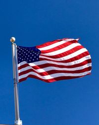 Low angle view of flags against clear blue sky