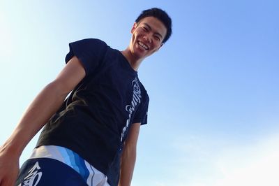 Low angle portrait of smiling woman against blue sky