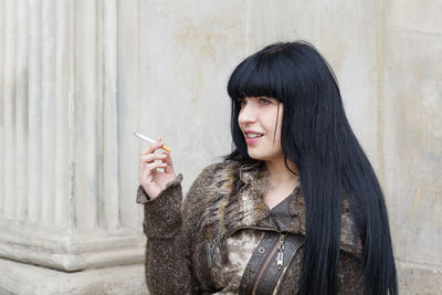 Beautiful woman smoking cigarette against wall