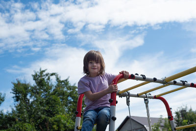 Child climbed the stairs on the playground and sits on the horizontal bar. girl exercising outside