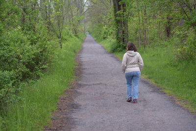 Rear view of woman walking on road in forest