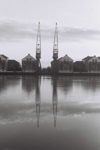 Cranes and buildings reflection in river thames against sky