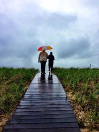 Rear view of woman walking on road against cloudy sky