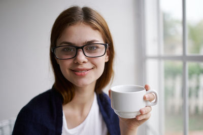 Portrait of young woman holding coffee cup at home