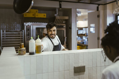 Smiling male chef reaching for oil bottle at commercial kitchen in restaurant