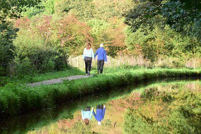 Rear view of man and woman walking on footpath by pond