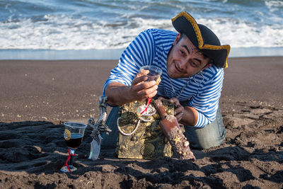 Pirate holding wineglass with treasure chest at beach