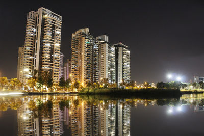 Reflection of illuminated buildings in lake against sky at night