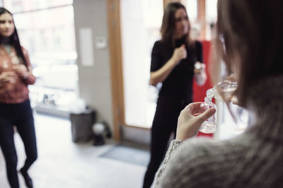 Rear view of female owner pouring liquid in bottle while standing with colleagues at perfume workshop