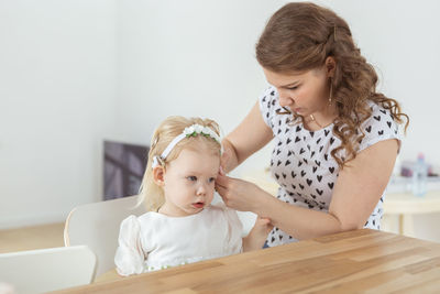 Mother adjusting daughter's hearing aid at home