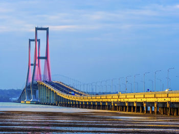 View of suspension bridge over sea against cloudy sky at dusk