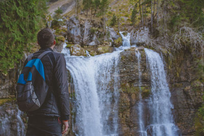 Rear view of man looking at waterfall in forest