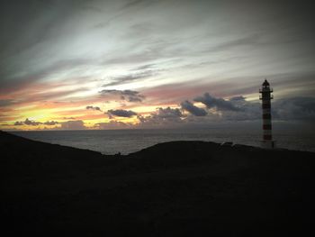 Lighthouse by sea against sky during sunset