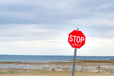 Road sign by sea against sky