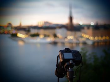 Close-up of camera on riverbank against sky at sunset