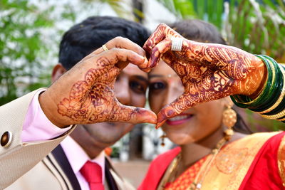 Close-up portrait of smiling newlywed couple making heart shape with hands