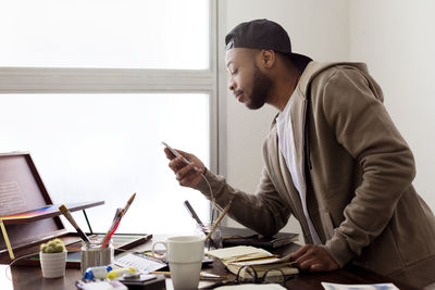 Side view of illustrator using smart phone at desk in creative office