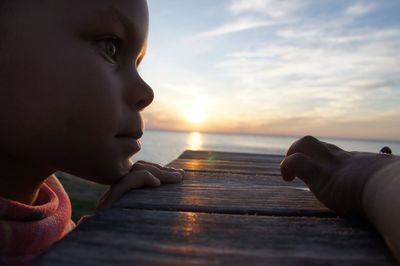 Close-up of boy looking at sea against sky during sunset