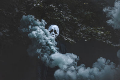 Spooky person wearing mask with distress flare against plants