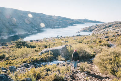 Rear view of man walking on mountain by lake against sky