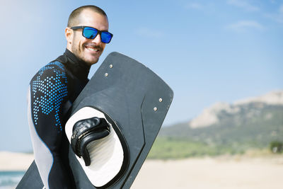 Portrait of man holding surfboard standing at beach