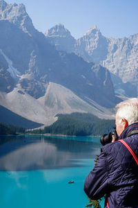 Rear view of man looking at lake against mountain