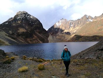 Rear view of woman standing on rock by lake against sky