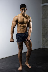 Portrait of shirtless muscular man standing against wall