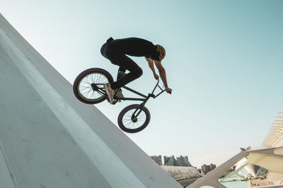 Man riding bicycle on built structure against sky