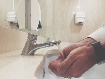 Cropped image of man washing hand under faucet