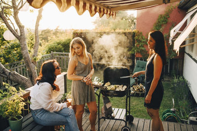Friends talking while grilling food on barbecue for dinner party in yard