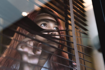 Close-up of woman looking away through blinds and window