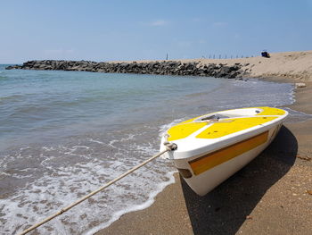 Yellow boat moored on beach against sky