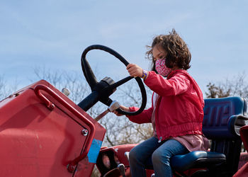 Girl in a mask pretending to drive a tractor at the county fair exhibit