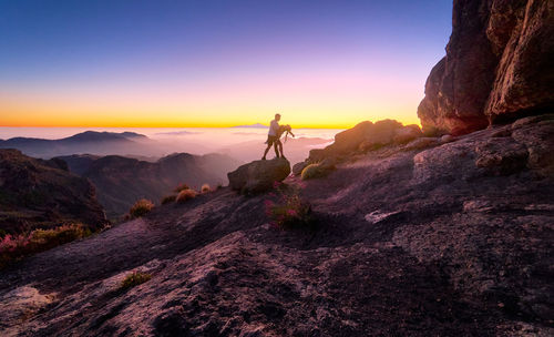 Man on rocks at mountain against sky during sunset