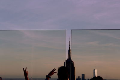 Silhouette people by building against sky during sunset