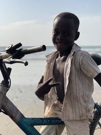 Portrait of boy showing peace sign while sitting on bicycle at beach